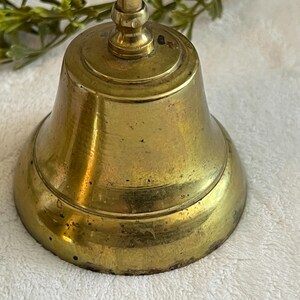 May include: A vintage brass bell with a rounded base and a handle. The bell has a tarnished, aged appearance, with visible wear and tear. The bell is likely used for decorative purposes or as a collectible item.