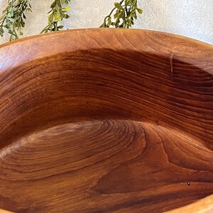 May include: A large, handcrafted wooden bowl with a rich, warm brown color. The bowl's interior showcases the natural wood grain, creating a unique and organic texture. The bowl's smooth, curved design suggests it is suitable for serving or display.