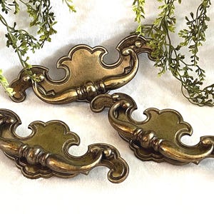 Op de afbeelding: Een set van drie keramische mokken met een gespikkelde, matte afwerking. De mokken zijn in de kleuren crème, lichtgrijs en donkergrijs. Elke mok heeft een eenvoudig, minimalistisch ontwerp en een afgeronde handgreep.