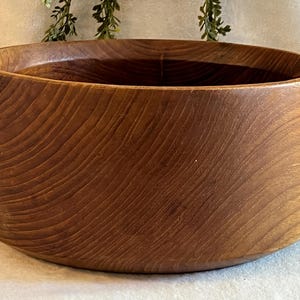 May include: A large, round wooden bowl with a rich, warm brown color. The bowl has a smooth, curved design and visible wood grain patterns. This decorative bowl is suitable for serving or display.
