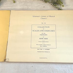 May include: An open book with a cream-colored page featuring the title "Collection of Scales and Exercises for the Pianoforte" by Henri Herz. The book is part of Schirmer's Library of Musical Classics, Vol. 170.