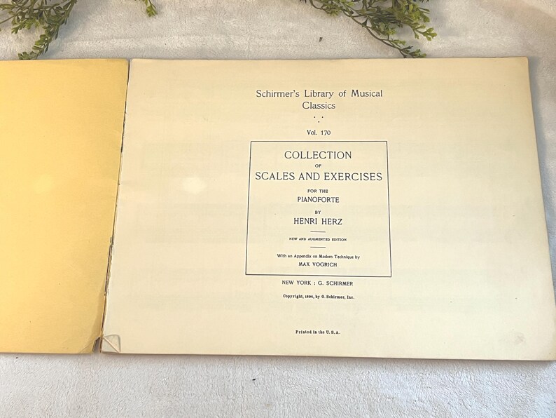 May include: An open book with a cream-colored page featuring the title "Collection of Scales and Exercises for the Pianoforte" by Henri Herz. The book is part of Schirmer's Library of Musical Classics, Vol. 170.