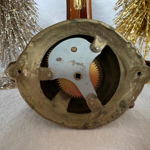 Op de afbeelding: Close-up van de achterkant van een messingbel met een zichtbaar tandwielmechanisme. De bel is rond en heeft een decoratief ontwerp.