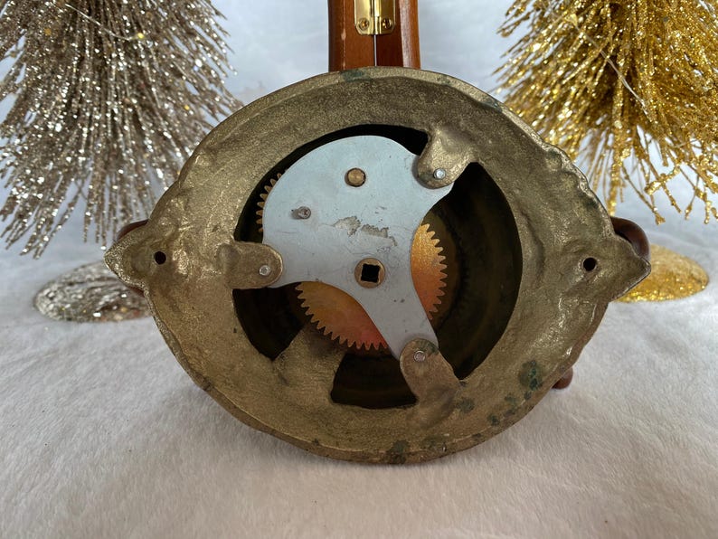 Op de afbeelding: Close-up van de achterkant van een messingbel met een zichtbaar tandwielmechanisme. De bel is rond en heeft een decoratief ontwerp.