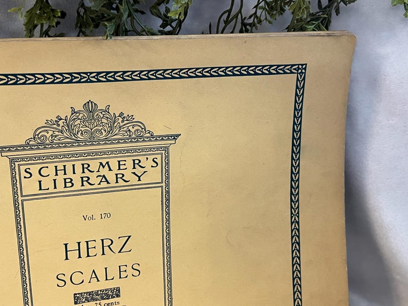 May include: A vintage book cover from Schirmer's Library, featuring the title "Herz Scales" in bold lettering. The cover is a light beige color with a decorative dark green border and ornate detailing. The book is volume 170.