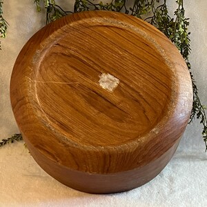 May include: A round, wooden bowl with a natural wood grain pattern. The bowl is a warm brown color and appears to be handmade. The bottom of the bowl is visible, showing the circular shape and the wood's texture.