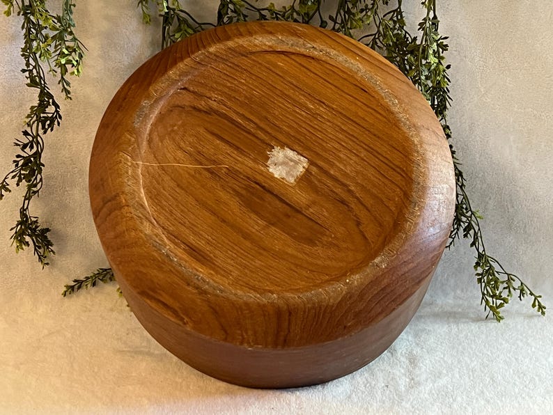 May include: A round, wooden bowl with a natural wood grain pattern. The bowl is a warm brown color and appears to be handmade. The bottom of the bowl is visible, showing the circular shape and the wood's texture.