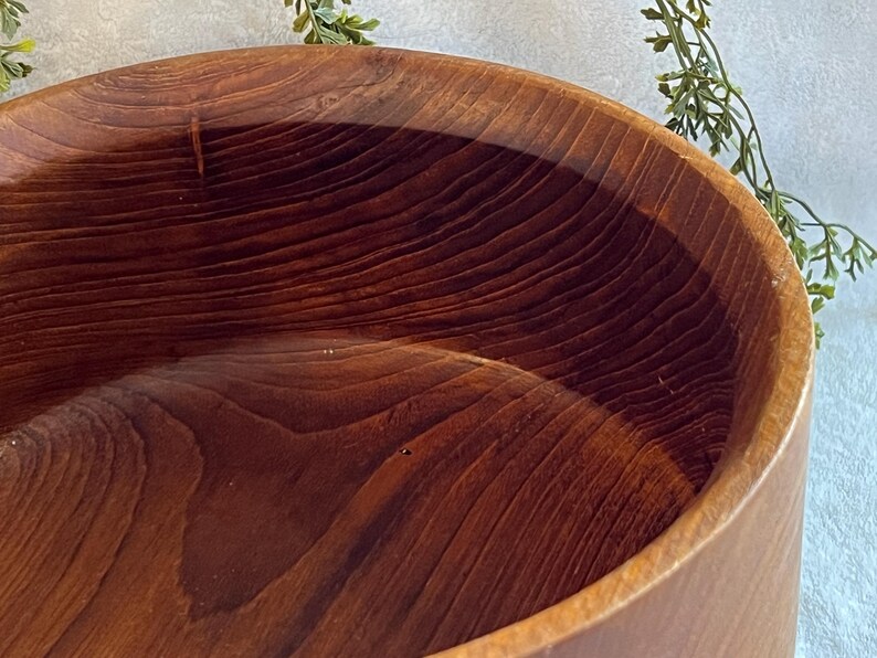 May include: A close-up of a large, round wooden bowl. The bowl is made of a rich, dark brown wood with visible grain patterns. The interior of the bowl is smooth and polished, reflecting the light. The bowl's exterior is a lighter shade of brown.