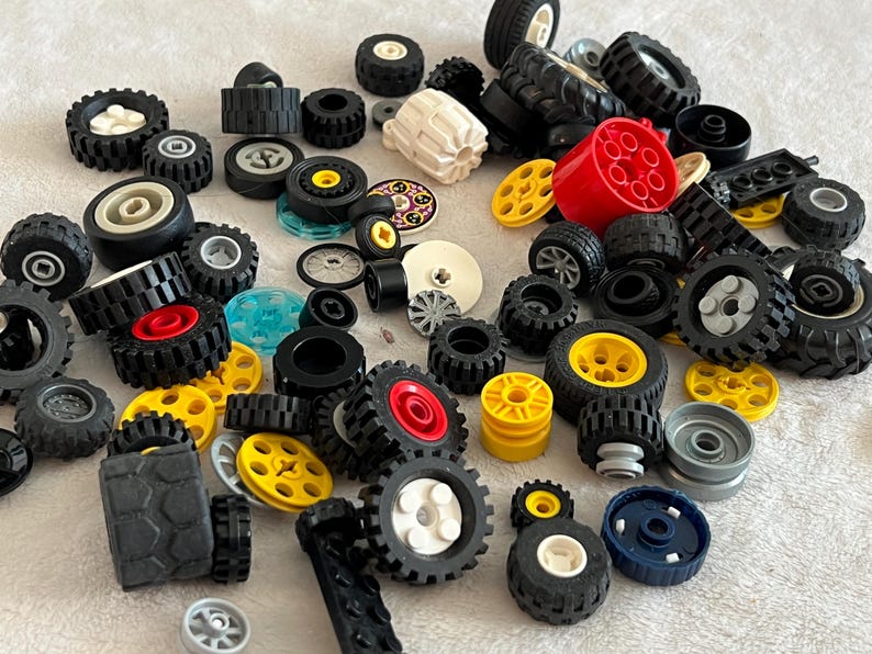 K&ouml;nnte beinhalten: Eine Sammlung verschiedener Spielzeugr&auml;der in Schwarz, Gelb, Rot und Wei&szlig;. Die Auswahl umfasst R&auml;der in verschiedenen Gr&ouml;&szlig;en und Designs sowie andere Bauelemente f&uuml;r Spielzeug.