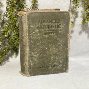 May include: An antique book titled "Advanced Arithmetic" by Morey, with a faded green cover. The book's cover shows wear and tear, with the words "State of Kansas" at the bottom. The book is a vintage educational item.