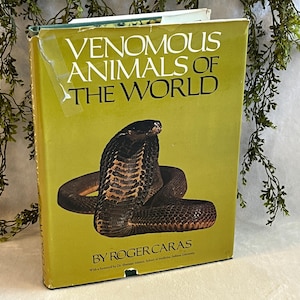 May include: A vintage book titled "Venomous Animals of the World" with a large illustration of a cobra on the cover. The book has a yellow-green cover with white text and is by Roger Caras.