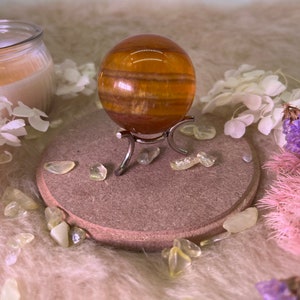 May include: A golden brown tiger's eye sphere on a metal stand. The sphere is surrounded by small, clear crystals on a brown wooden base.
