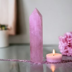 Puede incluir: Una punta de cristal rosa y una vela rosa sobre una mesa de vidrio con una flor rosa en el fondo.