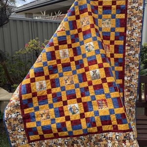 May include: A patchwork quilt featuring a repeating grid of mustard yellow and deep red squares, interspersed with square panels depicting various teddy bears. The quilt is bordered by a fabric print showcasing a dense pattern of teddy bears.