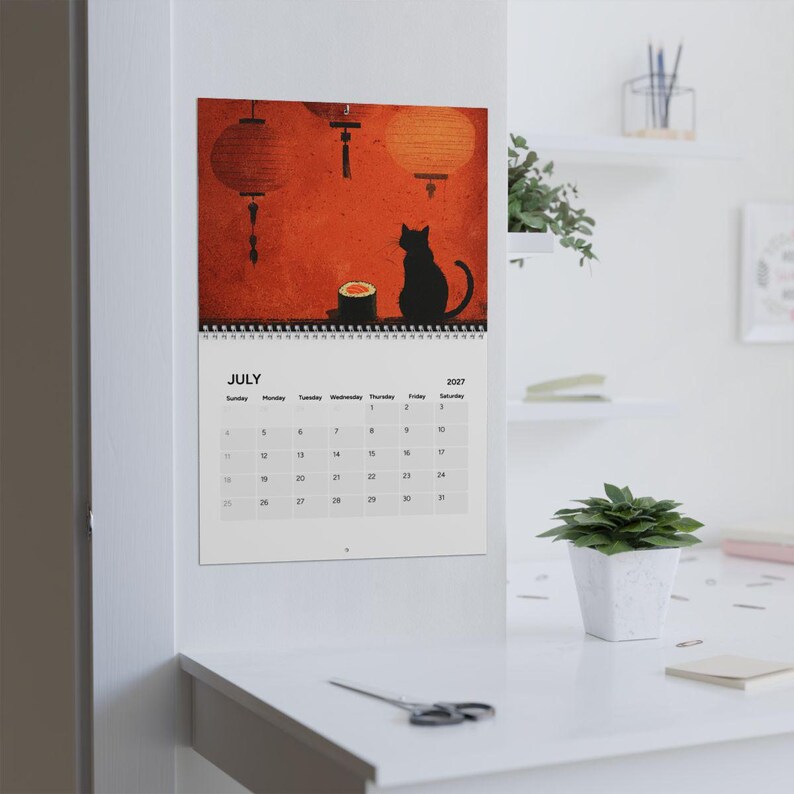 May include: A wall calendar for July 2027 featuring an illustration of a black cat sitting next to a piece of sushi under orange paper lanterns. The calendar grid displays the days of the month clearly with the month name July and year 2027.