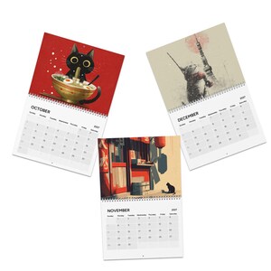 May include: Three wall calendars for the year 2027, each featuring a different cat-themed illustration. The October page shows a black cat eating ramen, November depicts a cat in a street scene, and December features a cat near a tower.