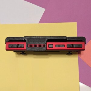 May include: A black and red handheld gaming console with buttons labeled L1, L2, R1, and R2. The console has a black plastic case with a textured surface and a red plastic faceplate.