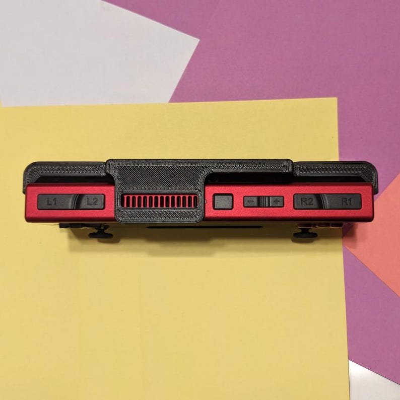 May include: A black and red handheld gaming console with buttons labeled L1, L2, R1, and R2. The console has a black plastic case with a textured surface and a red plastic faceplate.