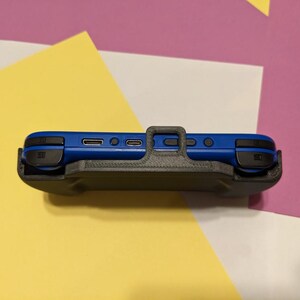 Może przedstawiać: Czarne ochronne etui do niebieskiej konsoli Nintendo Switch. Etui posiada wbudowaną podp&oacute;rkę i wycięcie na przyciski i porty konsoli.