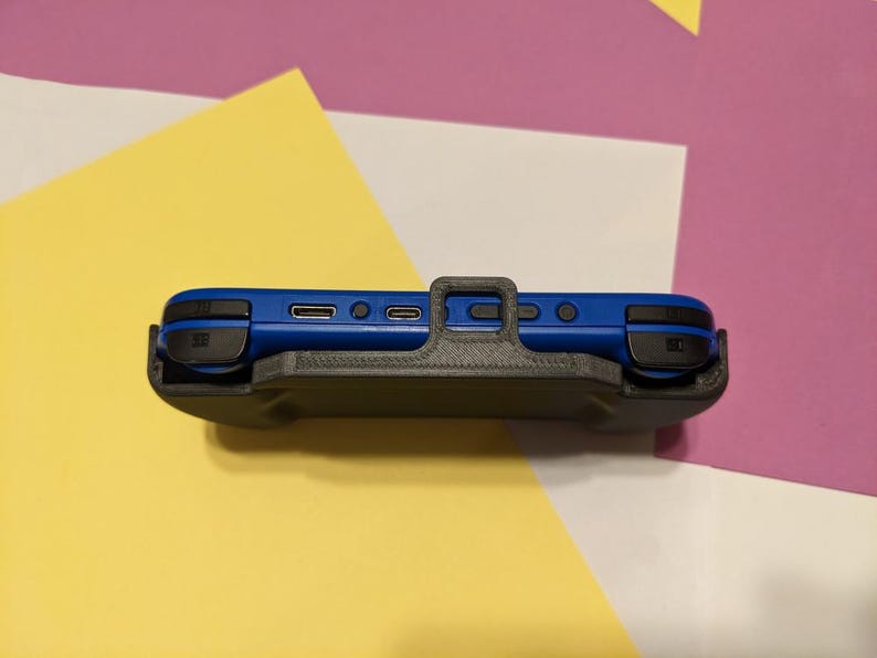 Może przedstawiać: Czarne ochronne etui do niebieskiej konsoli Nintendo Switch. Etui posiada wbudowaną podp&oacute;rkę i wycięcie na przyciski i porty konsoli.