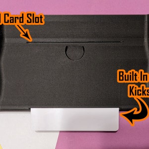 May include: Black protective case for a Nintendo Switch with a built-in storage slot for a kickstand card. The case has a slot for the kickstand card and a built-in storage compartment for the card.