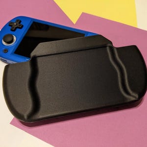 Puede incluir: Una funda protectora negra para un dispositivo de juego portátil azul. La funda tiene una superficie texturizada y un diseño curvo.