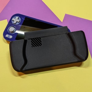 May include: A black protective case for a handheld gaming console, with a vent detail, rests on a yellow surface. A blue and black handheld gaming console is partially visible in the background, with a cross-shaped directional pad.