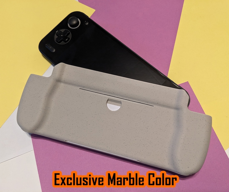 May include: A gray, textured case for a handheld gaming console. The case has a cutout for the console's screen and buttons. The text "Exclusive Marble Color" is printed on the case.