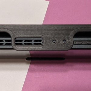 May include: Black Nintendo Switch console with a black 3D printed case attached to the back. The case has a raised lip to protect the screen.