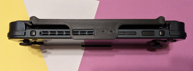 May include: Black Nintendo Switch console with a black 3D printed case attached to the back. The case has a raised lip to protect the screen.