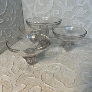 May include: Set of four clear glass candle holders with a decorative design. The holders are connected by a metal base.