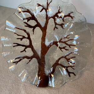 May include: A clear glass plate with a brown tree design. The plate has a scalloped edge and is perfect for serving snacks or desserts.