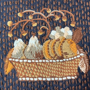 May include: A brown and white embroidered basket filled with pears and a cluster of brown and white flowers. The basket is on a dark blue background with a repeating pattern.