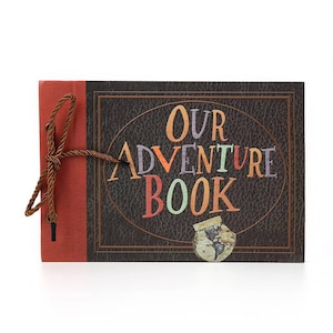 May include: A rectangular scrapbook titled "OUR ADVENTURE BOOK" with a brown leather-like cover and a red spine. The text is in colorful letters. A brown string ties the book together. A small illustration of a globe is on the front cover.