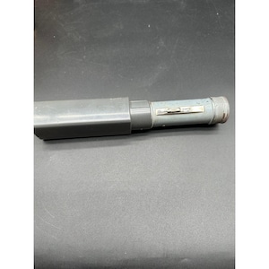May include: A grey metal torch with a cylindrical body and a textured end. The torch has a rectangular cover on the side. The switch is a small, silver-coloured bar.