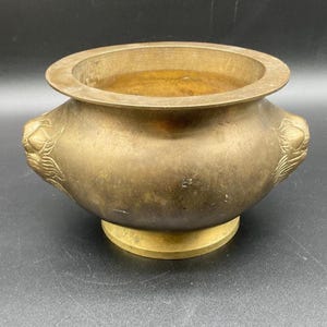 May include: A vintage brass incense burner with a wide, rounded body and a circular opening. The burner features decorative relief designs on the sides and rests on a circular base. The brass has a warm, aged patina.