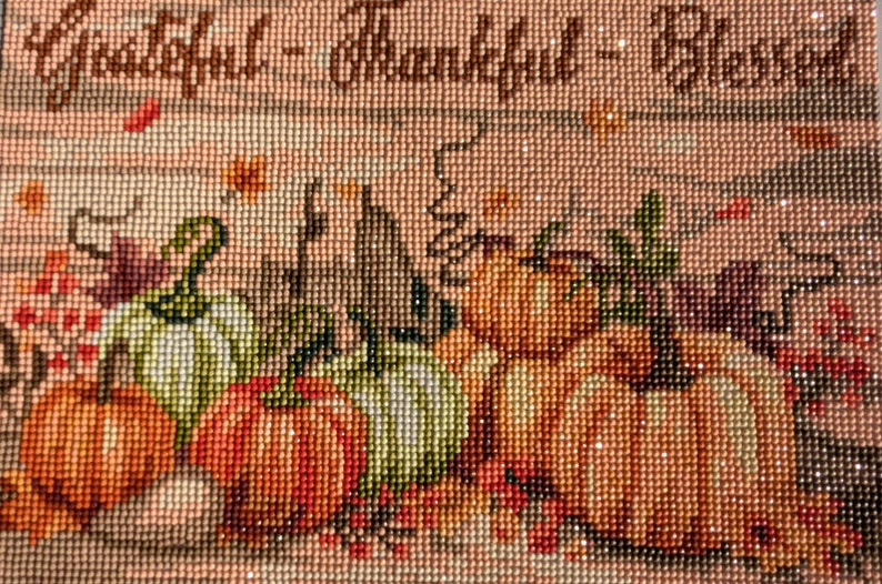 May include: A close-up of a beaded artwork depicting a still life of pumpkins and gourds with the text "Grateful - Thankful - Blessed".