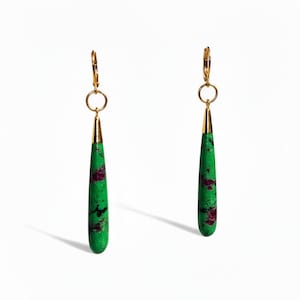 May include: A pair of gold-toned earrings with a green, teardrop-shaped stone. The green stone has red and black flecks. The earrings have a gold-toned lever back closure and a gold-toned cone-shaped top.