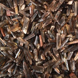 Puede incluir: Primer plano de una colección de cristales de cuarzo ahumado en bruto y natural. Los cristales varían en tamaño y forma, con una gama de tonos marrones y claros. Los cristales están agrupados, creando una apariencia texturizada y orgánica.