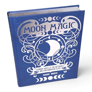 May include: A blue hardcover book titled Moon Magic: Lunar Spells to Attract an Enchanted Life by Marie Bruce. The cover features silver foil detailing, including a central crescent moon icon, intricate swirling patterns, and lunar phase symbols.