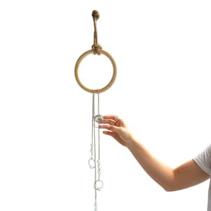 May include: A wooden ring jewellery organiser suspended by a natural rope. Several silver necklaces with geometric and pearl-like charms hang from the ring. A hand is reaching towards the necklaces.