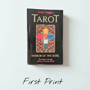 Op de afbeelding: Een zwart boek met de titel "TAROT" van Gerd Ziegler. De omslag toont een kleurrijk kruisontwerp op een patroonachtergrond. De titel "MIRROR OF THE SOUL" staat onder de hoofdtitel, met "First Print" onderaan.