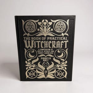 May include: A hardback book with a black cover and gold lettering and embellishments. The title reads "THE BOOK OF PRACTICAL WITCHCRAFT". The cover design includes stars, hearts, and floral patterns. The author is Pamela Ball.