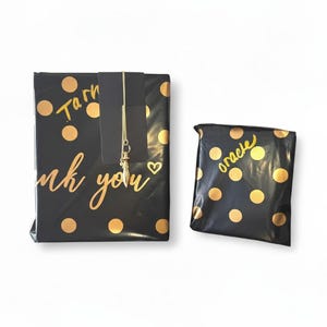 Op de afbeelding: Twee zwarte pakketten met gouden stippen. Op één pakket staat in gouden letters "Thank you", op het andere het woord "oracle". Een gouden ketting met een bedel hangt aan het grotere pakket.
