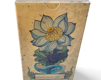 Puede incluir: Una caja rectangular para cartas de tarot con un fondo beige texturizado. La parte frontal presenta una gran ilustración detallada de una flor de loto con pétalos azules y blancos y un centro amarillo. El texto dice Botanica Oculta Tarot y Dark Synevyr.