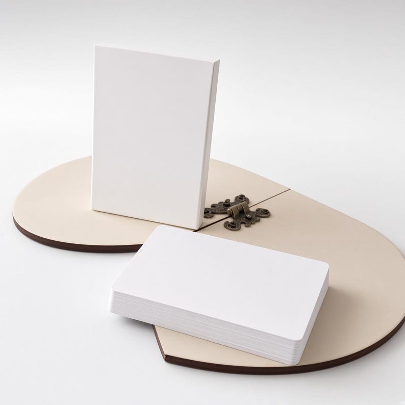 May include: A stack of blank white rectangular cards and a single upright white card positioned on a light beige, heart-shaped wooden base. The base features a dark brown edge and is connected by a decorative, ornate bronze-colored metal hinge.