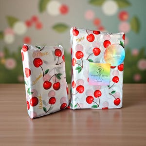 May include: Two wrapped packages with cherry-printed paper. One package has the words "Oracle", "Adored", and "Blessed" printed on it. The other package has the word "Tarot" and a sticker that says "I AM WORTHY" and "Modern Meems".