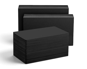 May include: A stack of rectangular black cards positioned in the foreground, with two larger, empty black rectangular boxes placed directly behind the stack. The cards and boxes feature a solid, matte black finish with no visible text or patterns.