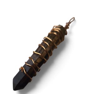 May include: A long, hexagonal, dark brown and black crystal point pendant wrapped in a spiraling copper-colored wire. The wire forms a small loop at the top for hanging. The crystal has a smooth, polished surface with visible natural banding.