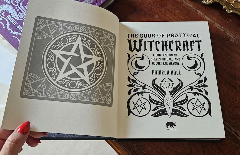 May include: An open book titled "The Book of Practical Witchcraft" by Pamela Ball. The left page has a grey pentagram design. The right page features the title in black with decorative illustrations.